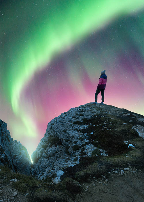 Person standing on a bluff looking at northern lights