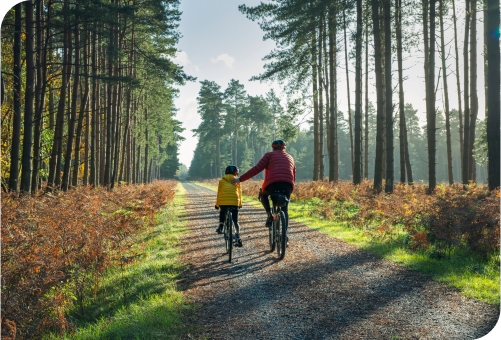 Parent and child riding bikes down a wooded gravel path.